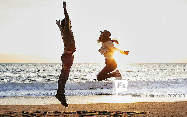 Carefree boyfriend and girlfriend enjoying while jumping against sea