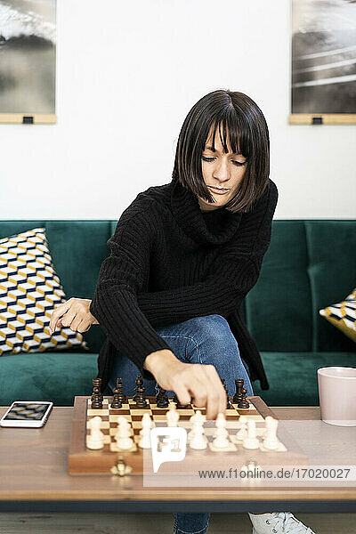 Junge Frau mit Konzentration beim Schachspielen im Wohnzimmer