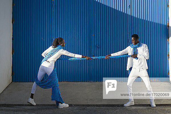 Smiling couple pulling blue fabric against corrugated wall on street