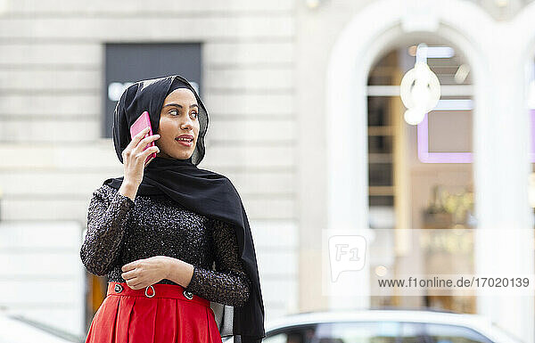 Porträt einer jungen schönen Frau mit schwarzem Hidschab  die mitten auf der Straße mit einem Smartphone telefoniert