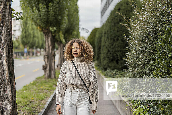 Schöne junge Frau schaut weg  während sie auf dem Fußweg in der Stadt spazieren geht