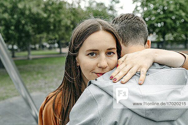 Lächelnde Freundin umarmt ihren Freund in einem öffentlichen Park