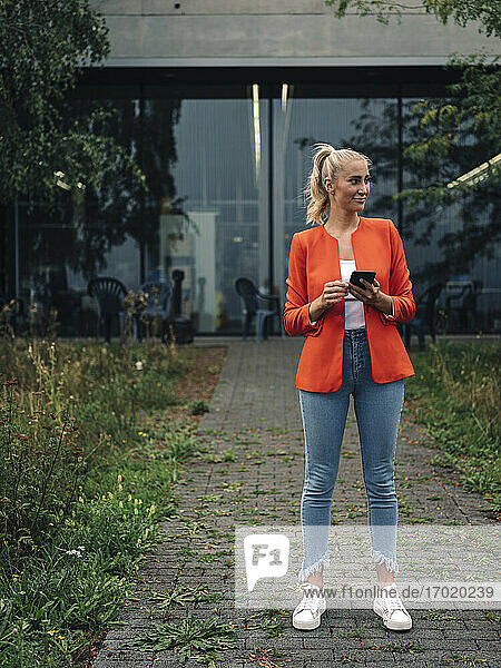 Junge Unternehmerin mit Smartphone im Firmengarten stehend