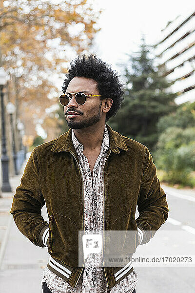 Stilvoller erwachsener Mann mit Sonnenbrille und Händen in den Taschen auf der Straße stehend