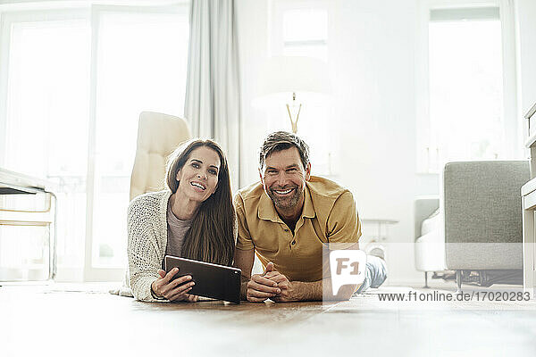 Lächelnder reifer Mann und Frau mit digitalem Tablet auf dem Boden liegend in einer Wohnung