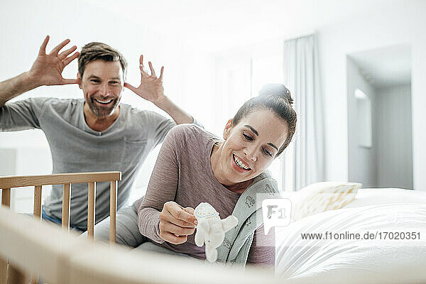 Playful mature couple sitting by crib on bed at home