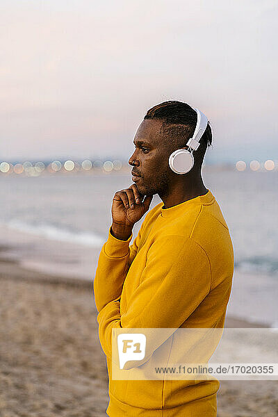 Mittlerer erwachsener Mann mit Kopfhörern  der Musik hört  während er am Strand steht