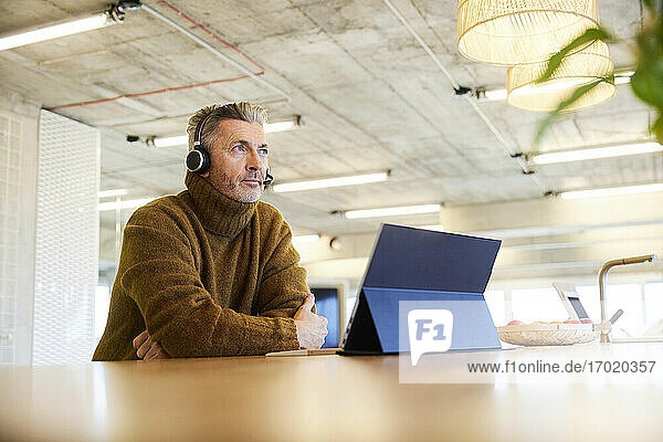 Nachdenklicher Geschäftsmann mit Headset und digitalem Tablet  der im Büro sitzt und wegschaut