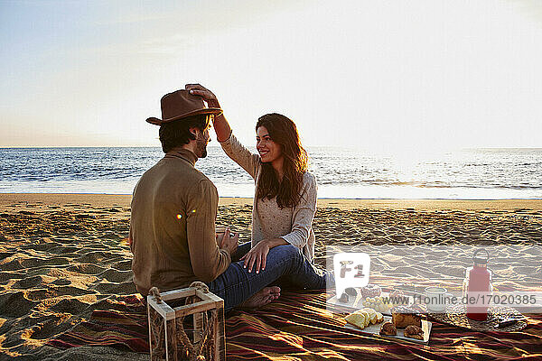 Frau spielt mit Hut und sitzt neben einem Mann am Strand