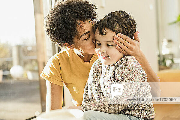 Mutter küsst ihren Sohn  während sie zu Hause sitzt
