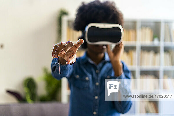 Young woman wearing virtual reality touching while standing at home