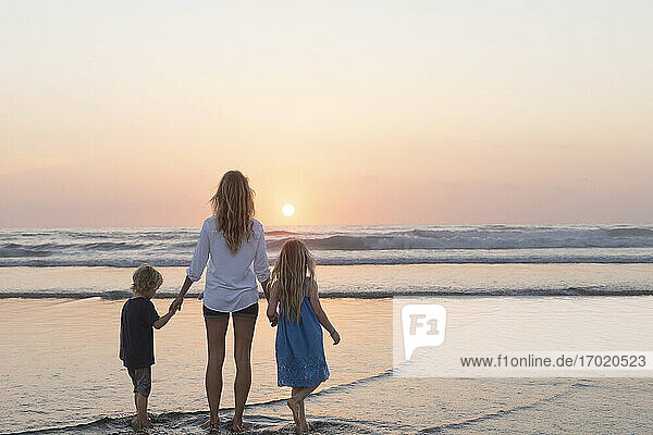 Mother and children looking at sunset view while standing at beach
