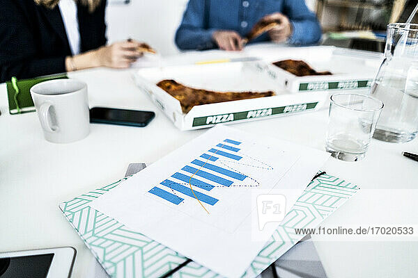 Geschäftsleute essen Pizza im Büro während der Pause  Dokumente im Vordergrund