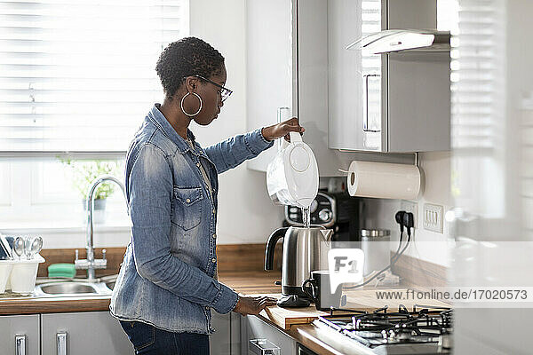 Frau gießt Wasser in einen Wasserkocher in der Küche