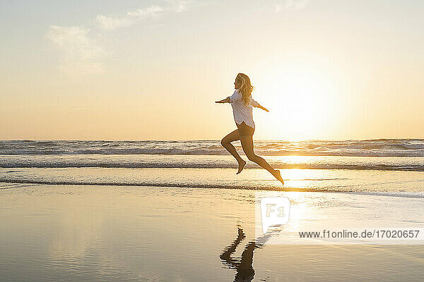 Happy woman with arms outstretched jumping against sea