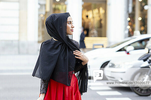 Porträt einer jungen schönen Frau mit schwarzem Hidschab  die mitten auf der Straße posiert