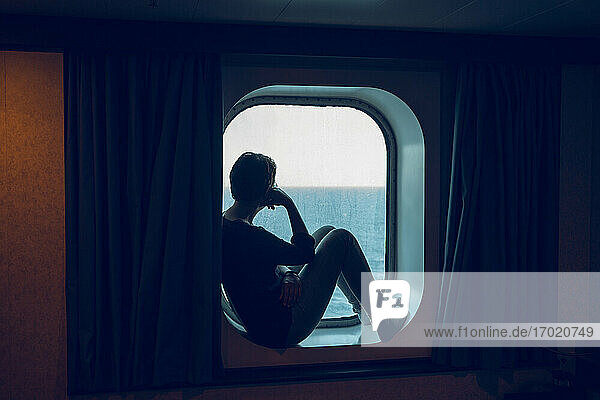 Frau betrachtet die Aussicht  während sie am Schiffsfenster sitzt