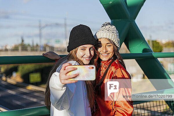 Lächelnde Freunde  die ein Selfie mit ihrem Mobiltelefon machen  während sie auf einer Brücke stehen
