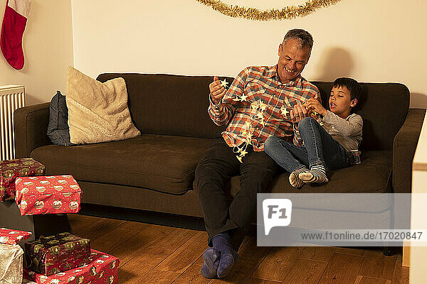 Father and son playing with Christmas lights while sitting on sofa at home