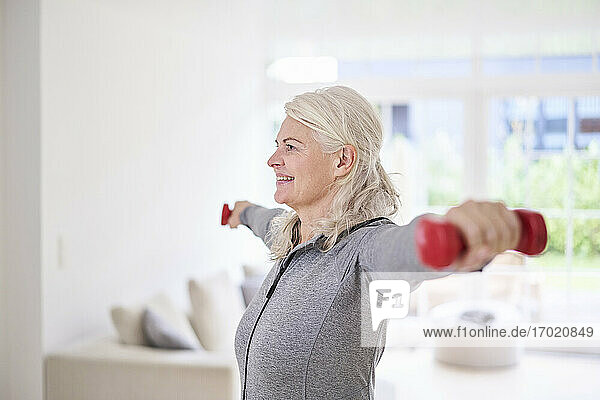 Smiling senior woman exercising with dumbbells at home