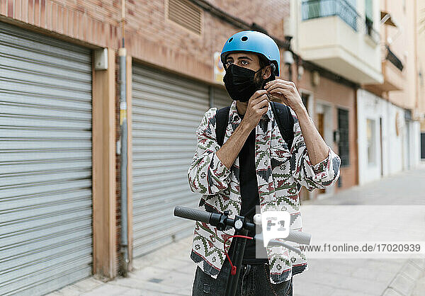 Junger Mann mit Gesichtsmaske auf einem elektrischen Roller in der Stadt