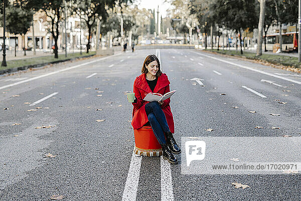 Glückliche junge Frau liest ein Buch und hält eine Kaffeetasse auf der Straße