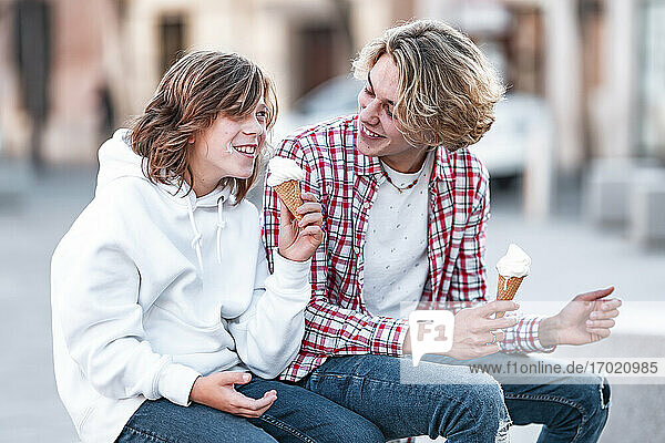 Lächelnder Junge isst Eis  während er neben einem Mann im Freien sitzt