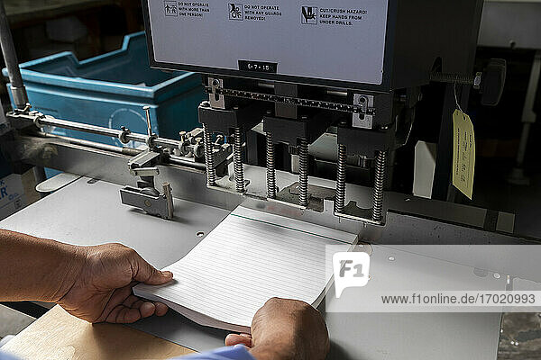 Männlicher Angestellter  der ein Bündel Papiere in einer Druckmaschine in einem Geschäft anpasst