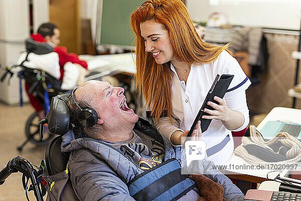 Eine lächelnde Krankenschwester zeigt einem glücklichen behinderten Mann im Pflegeheim ein digitales Tablet