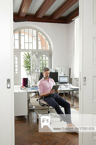 Älterer Geschäftsmann  der ein digitales Tablet benutzt  während er in einer Bürokabine sitzt