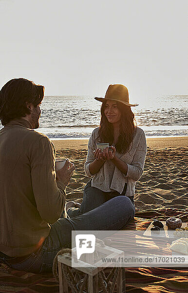 Junges Paar trinkt am Strand sitzend Kaffee
