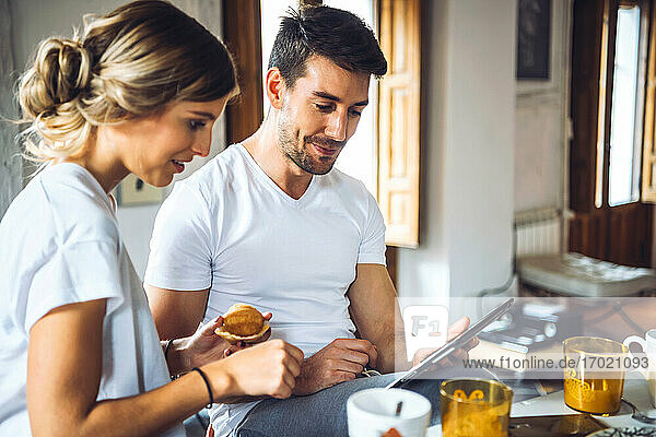 Junges Paar schaut beim Frühstück zu Hause auf ein Tablet