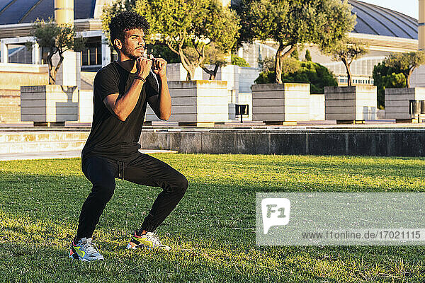 Young man exercising while standing on grassy land in park during sunset