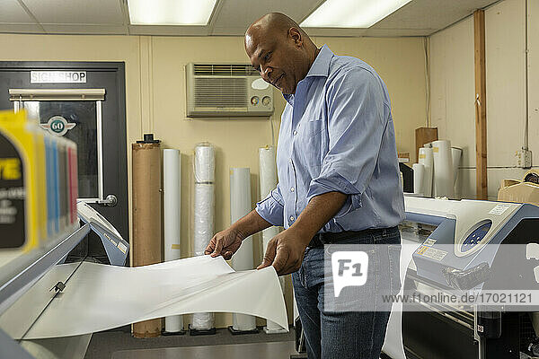 Lächelnde Aufsichtsperson  die Papier in die Druckmaschine einlegt  während sie im Geschäft arbeitet