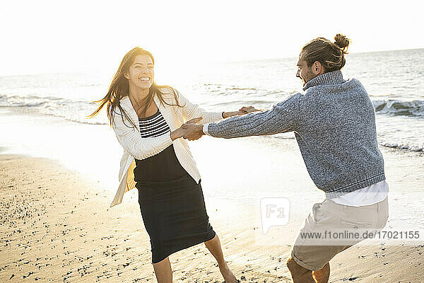 Fröhliches junges Paar hält sich an den Händen und genießt den sonnigen Tag am Strand
