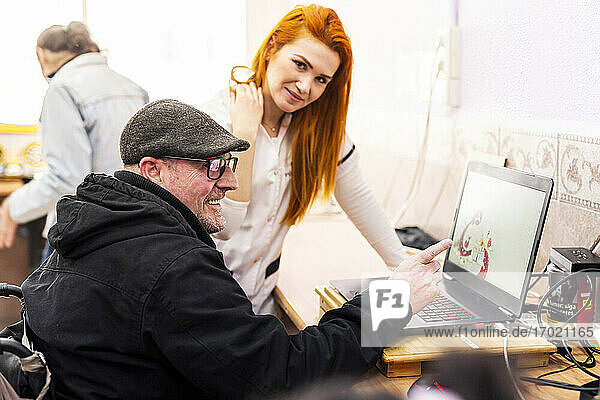 Lächelnder Mann  der von einer Betreuerin im Behindertenzentrum einen Laptop benutzt