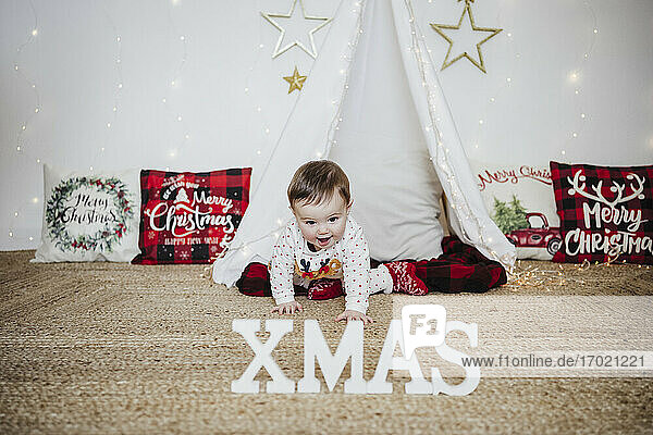 Lächelndes kleines Mädchen krabbelt zu Weihnachten auf dem Boden in Richtung XMAS-Text