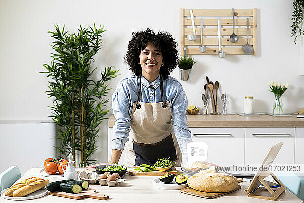 Porträt einer jungen Frau  die sich auf den Küchentisch stützt und in die Kamera lächelt