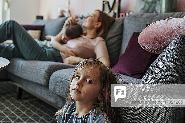 Mutter mit älterer Tochter  während die Schwester unter der Couch im Wohnzimmer sitzt