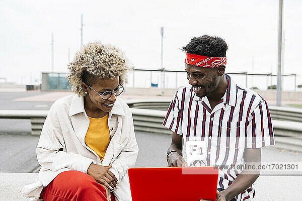 Lächelnde Freunde  die auf einer Bank sitzend einen Laptop benutzen