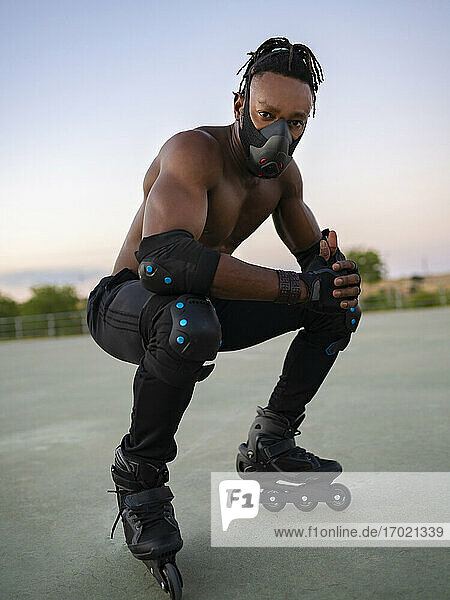 Sportsman wearing protective face mask and roller skate crouching on ground