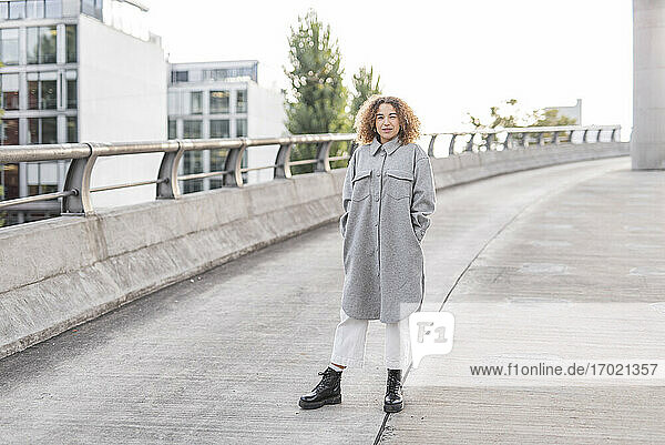 Beautiful young woman with curly blond hair standing on bridge in city