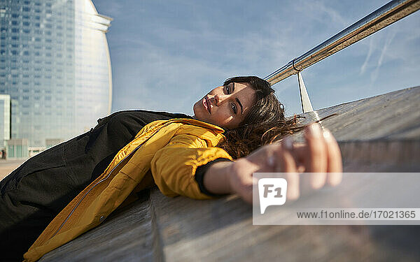 Carefree woman lying on retaining wall at pier during sunny day