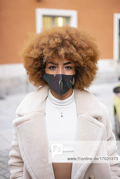 Mittlere erwachsene Frau mit Afro-Haar  die eine Gesichtsmaske trägt und an einem Gebäude steht