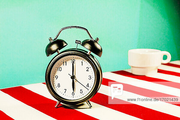 Studio shot of alarm clock standing on white and red striped pattern