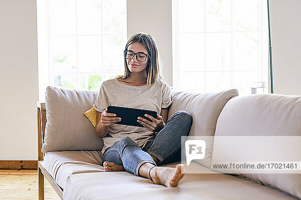 Entspannte brünette Geschäftsfrau  die auf dem Sofa sitzt und ein digitales Tablet im Wohnzimmer zu Hause benutzt