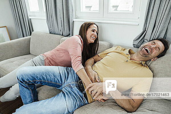 Happy mature woman tickling man while sitting on sofa at home