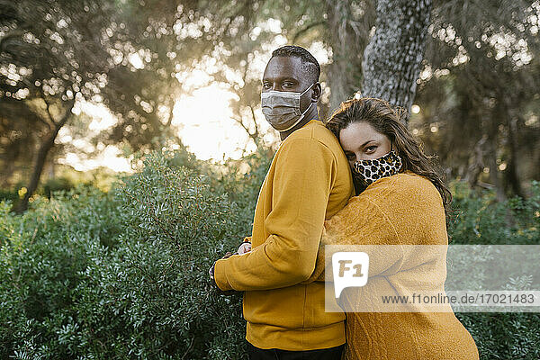 Frau mit Gesichtsmaske umarmt Mann während Covid-19 im Wald stehend