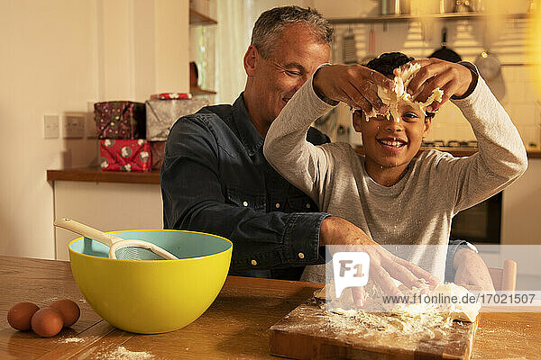 Vater und Sohn kneten Teig auf dem Tisch  während sie in der Küche sitzen