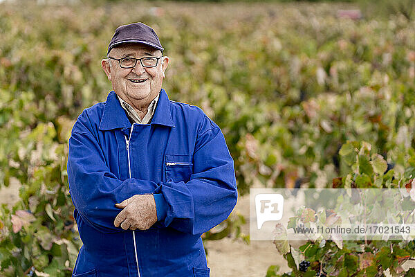Lächelnder älterer Mann mit verschränkten Armen vor einer Weinrebenfarm